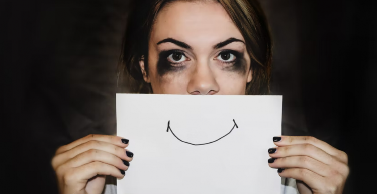 A sad lady holding up a card in front of her face with a smile drawn on it