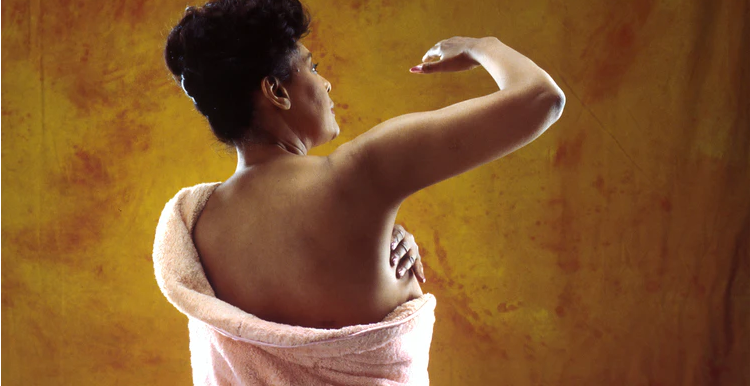 A woman with her back turned, examining her breast for signs of cancer