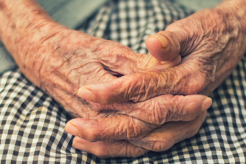 Close up image of an elderly woman's hands clasped on her knees