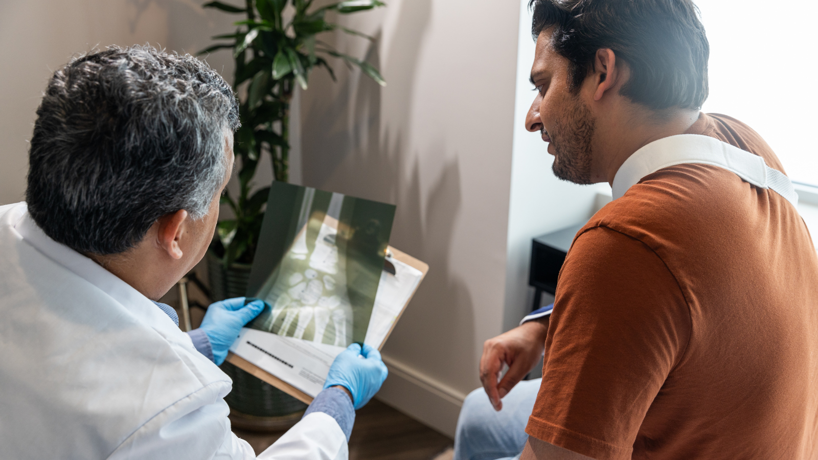 A photo of a doctor showing a patient with a sling an x-ray of a hand.