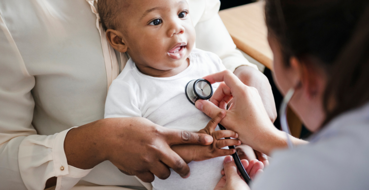 A photo of a baby being held by a parent as a doctor checks their heartbeat