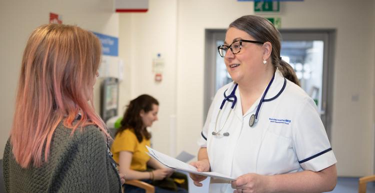 A photo of medical professional talking to a woman in a waiting room.