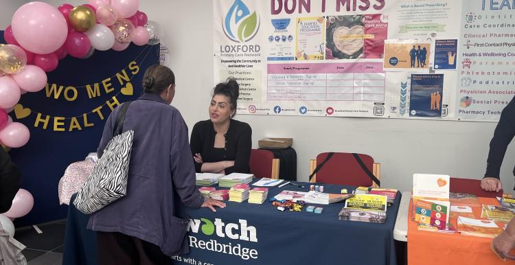A photo of a Healthwatch Redbridge stall next to a sign that reads 'Women's Health'.