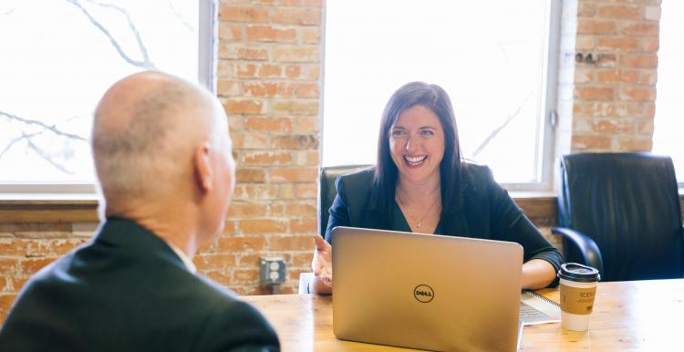 man sat across interview table from female interviewer with laptop