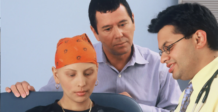 A woman with no hair wearing a head scarf, with her husband standing behind her