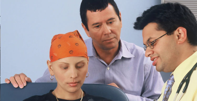 A woman with no hair wearing a head scarf, with her husband standing behind her 