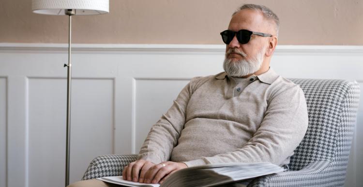 A blind man sat on an armchair reading braille