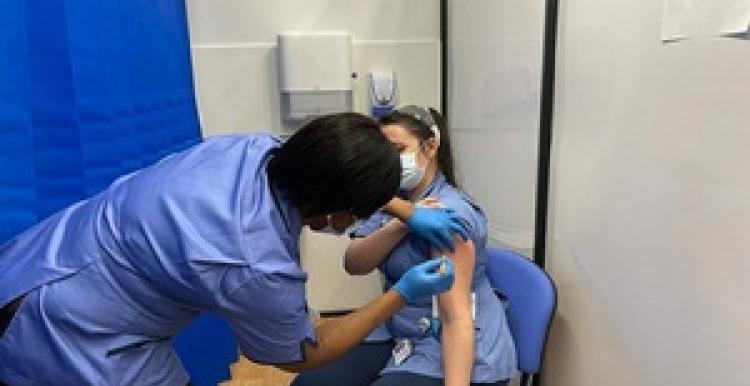 A female nurse giving another female nurse a vaccination