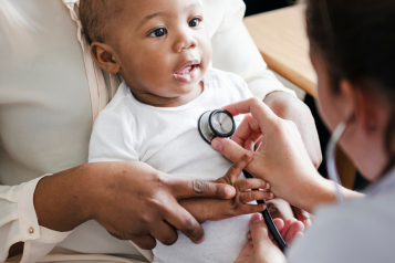 A photo of a baby being held by a parent as a doctor checks their heartbeat