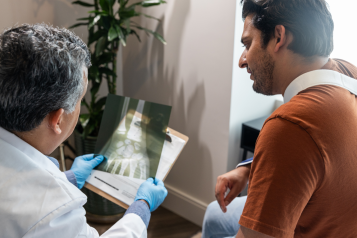 A photo of a doctor showing a patient with a sling an x-ray of a hand.