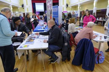 A photo of a busy hall with stalls and people walking around. 