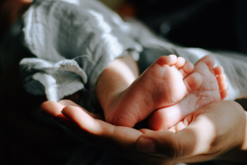 Close up of a mother's hands supporting the feet of a new born baby