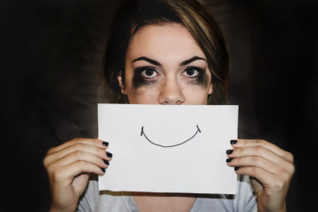 A sad lady holding up a card in front of her face with a smile drawn on it