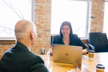 man sat across interview table from female interviewer with laptop