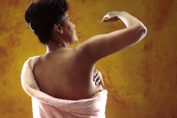 A woman with her back turned, examining her breast for signs of cancer