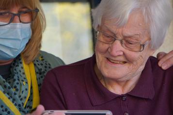 Smiling female carer in blue hospital mask alongside elderly female service user