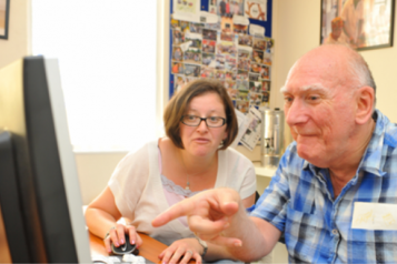 A woman showing a man with learning disabilities some information on a computer screen