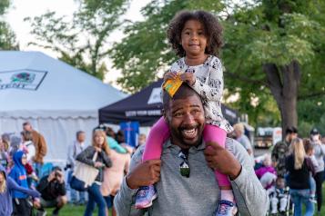 little girl sitting on her dad's shoulders at an outdoor festival