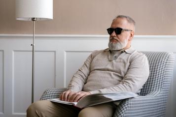 A blind man sat on an armchair reading braille