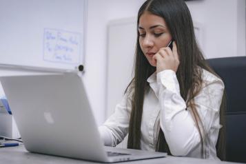 A young lady looking at her laptop whilst making a mobile call