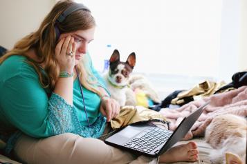 A young woman sat on her bed with her laptop