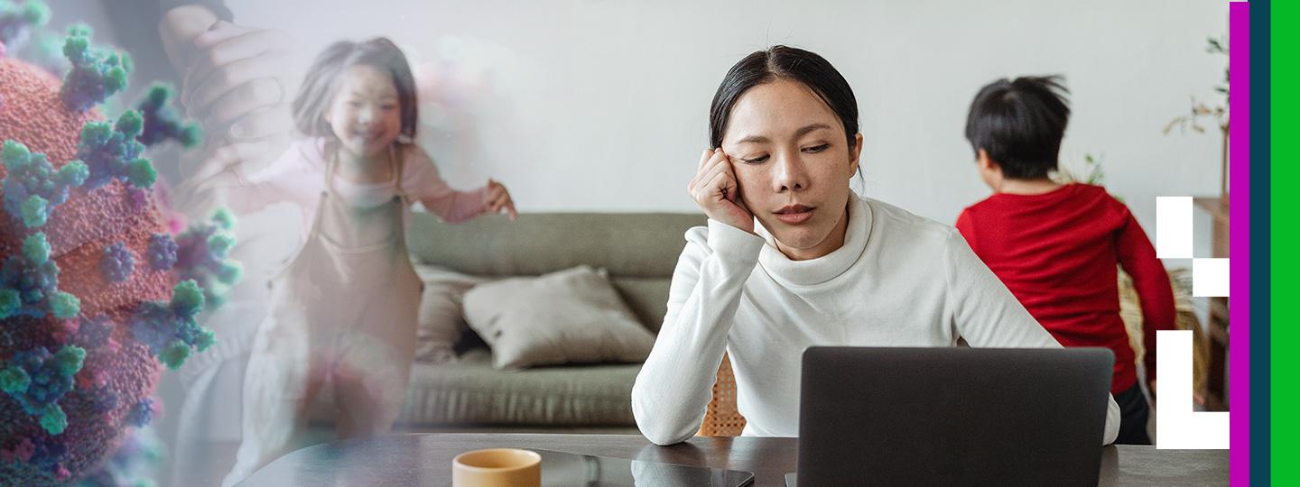 A mother looking tired, in front of a laptop, with her two kids running around