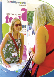Healthwatch Redbridge Volunteer Coordinator at a stall, talking to a member of public